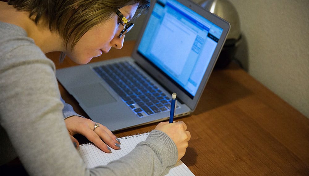 Woman studying with laptop, pad and paper