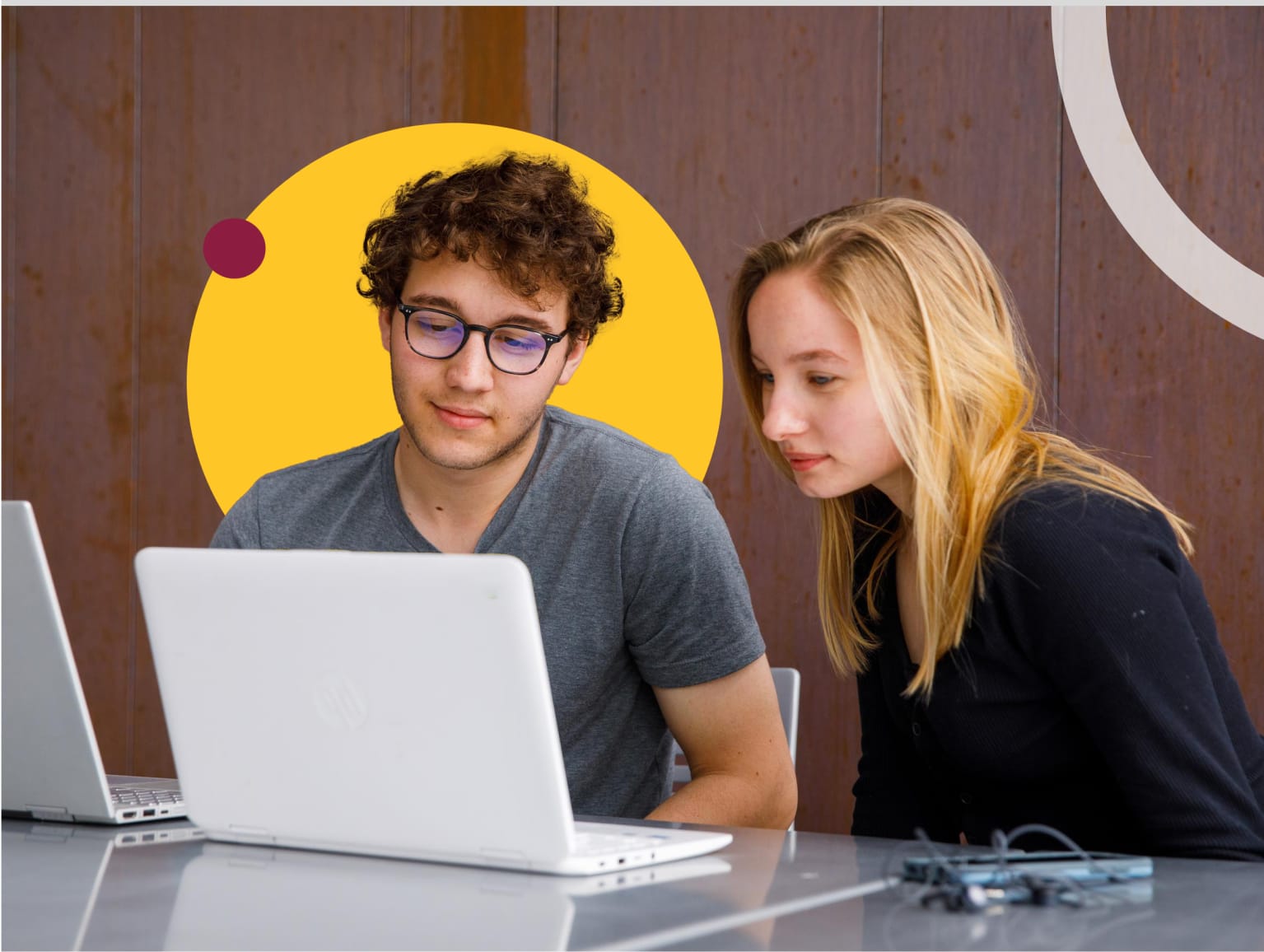 Two students sitting at a desk and looking at laptops