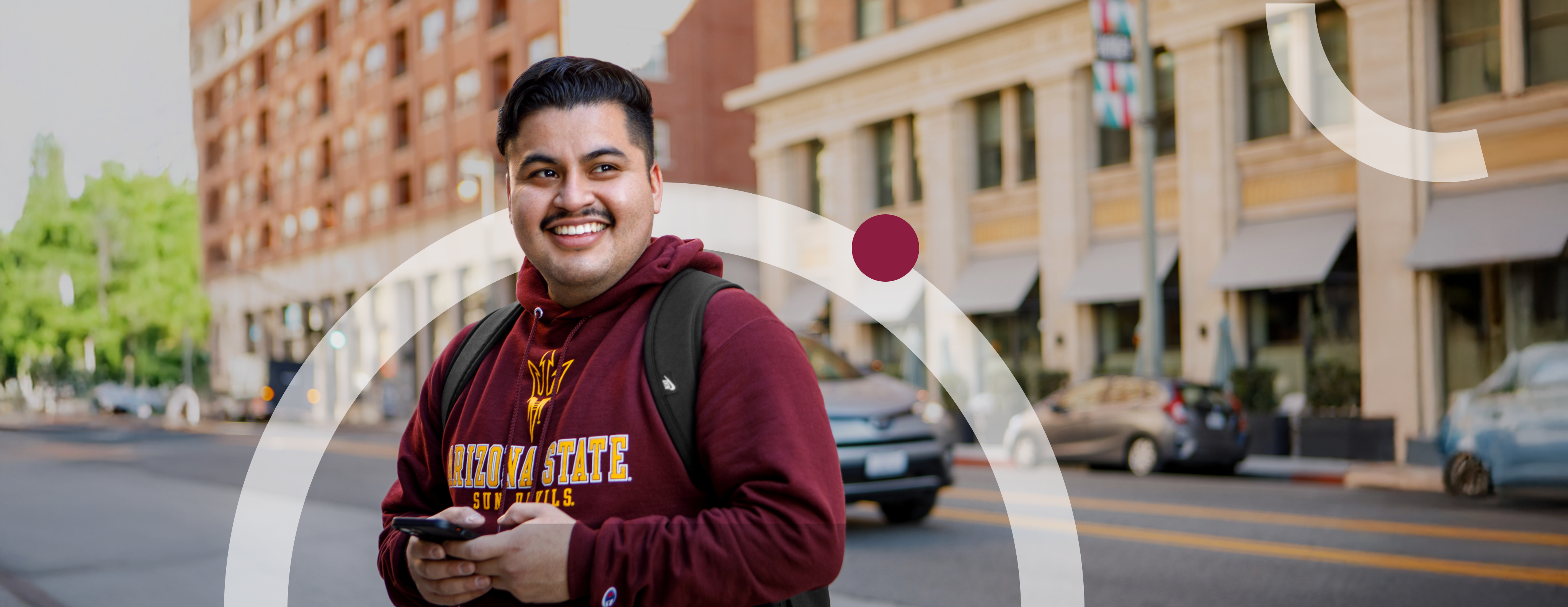 Hispanic man in ASU sweatshirt texting on the street